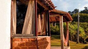 A rustic building with a tiled roof, a window with curtains, and a stone pathway leading to a covered area. - Serra a vista chalés (Prados)