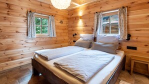 A wooden cabin bedroom with a bed, two windows with curtains, a hanging light fixture, and a nightstand. - 'Chalet Kaisereck' with Terrace & Wi-Fi (Reit im Winkl)
