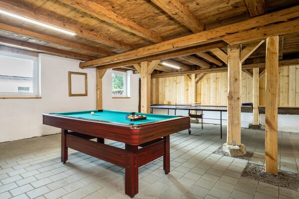 Une table de billard recouverte d’un drap vert, avec des poutres en bois et un sol carrelé.