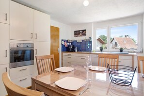 A modern kitchen with white cabinets, a built-in oven, and a dining area with a wooden table and chairs.