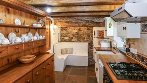 Een keuken met houten kastjes, een stenen muur, een inbouwoven en een spoelbak.