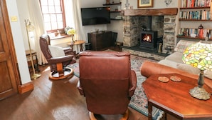 Een gezellige woonkamer met een open haard, een leren fauteuil, bank en een boekenplank vol boeken.