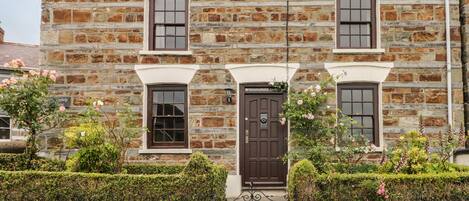 A stone building with a central entrance, flanked by two windows and a door.