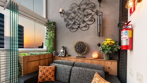 A modern living room with a sofa, patterned cushions, a decorative wall piece, a small Buddha statue, a plant, and a fire extinguisher. - Summit Pinheiros by Okaeri Home Aparts (São Paulo)