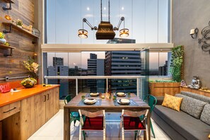 Een moderne keuken met een eethoek, houten kasten en een groot raam met uitzicht op een stadsbeeld.