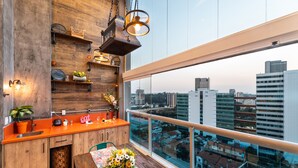 A modern kitchen with wooden cabinets, a large window with a city view, and a dining area with a floral table runner. - Summit Pinheiros by Okaeri Home Aparts (São Paulo)