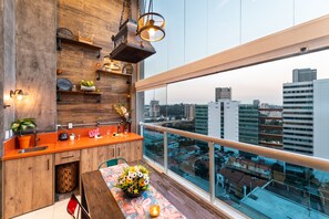 Uma cozinha moderna com armários de madeira, uma janela grande com vista para a cidade e um espaço de refeições com toalha de mesa estampada.