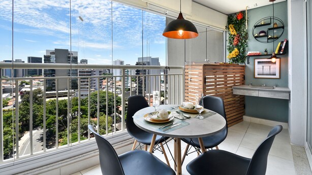 A dining area with a balcony overlooking a cityscape, featuring a round table, chairs, and a hanging light fixture. - Summit Pinheiros by Okaeri Home Aparts (São Paulo)