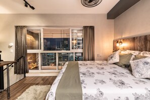 Un dormitorio moderno con una cama grande, vista de la ciudad por la noche y un balcón con cortinas.