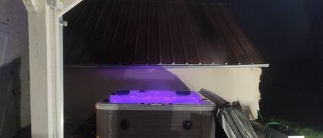 Een jacuzzi onder een overdekte patio met een metalen dak, een betonnen vloer en een metalen stoel.