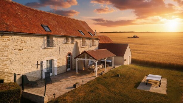 Une ferme en pierre avec un patio couvert, une grange et un champ en arrière-plan.