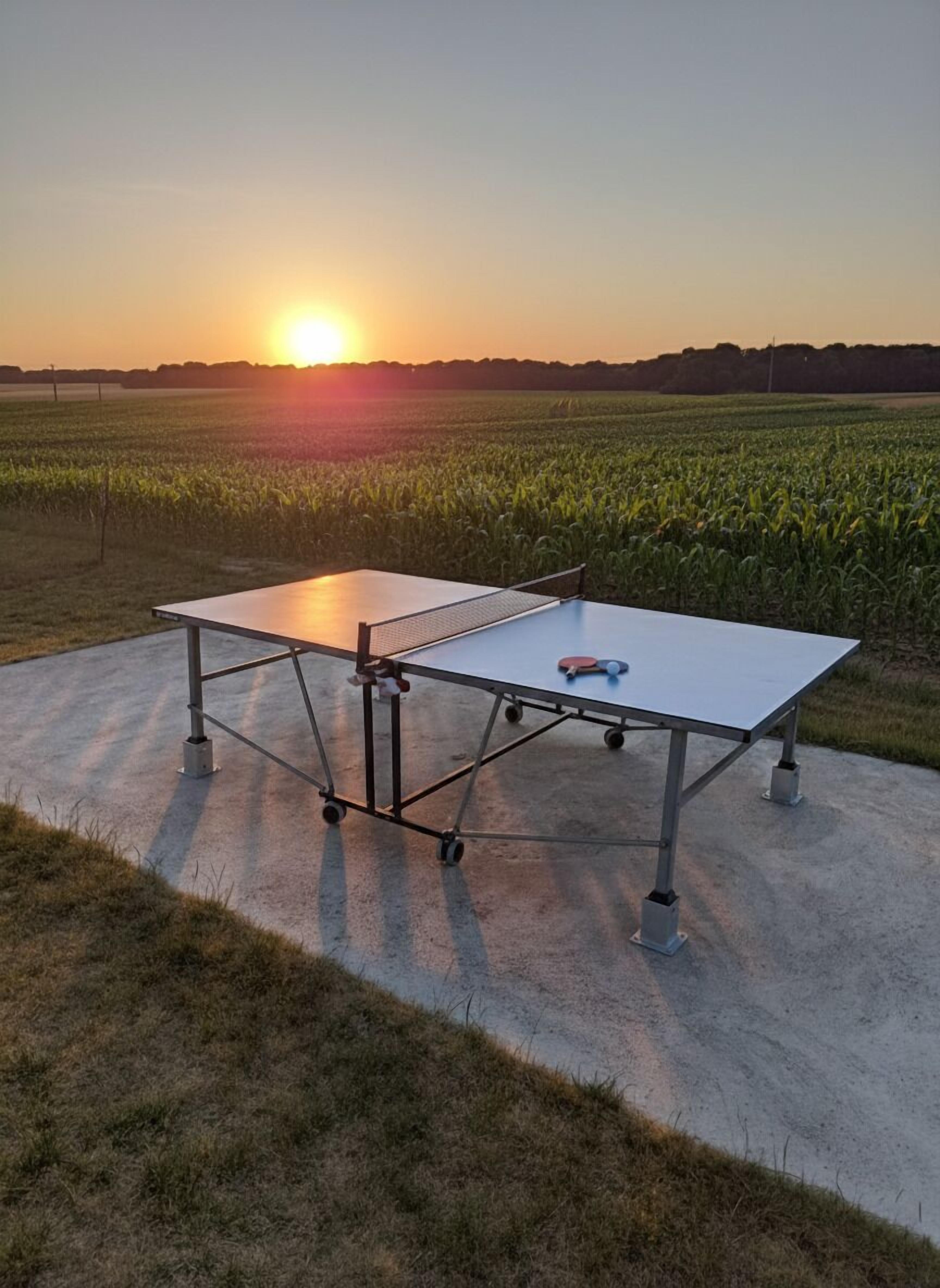 Two ping pong tables set up outdoors with a sunset in the background.