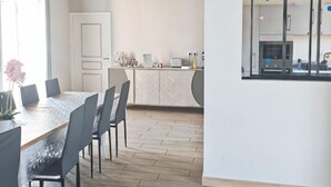 Une cuisine moderne dotée d’un îlot central, d’un coin repas avec une longue table et des chaises, et d’une grande fenêtre agrémentée d’éléments décoratifs.