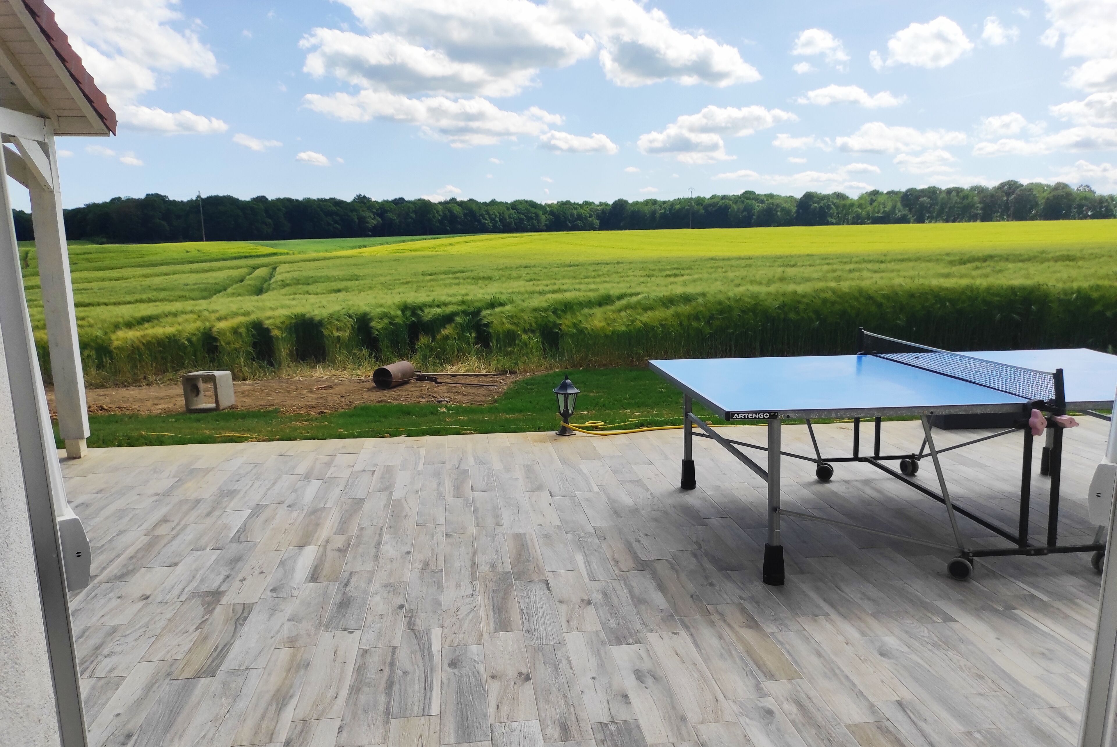 A ping pong table on a patio with a view of a green field.