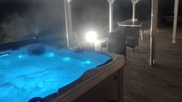 Un bain à remous doté d’un éclairage bleu, entouré d’une terrasse en bois et de mobilier d’extérieur.