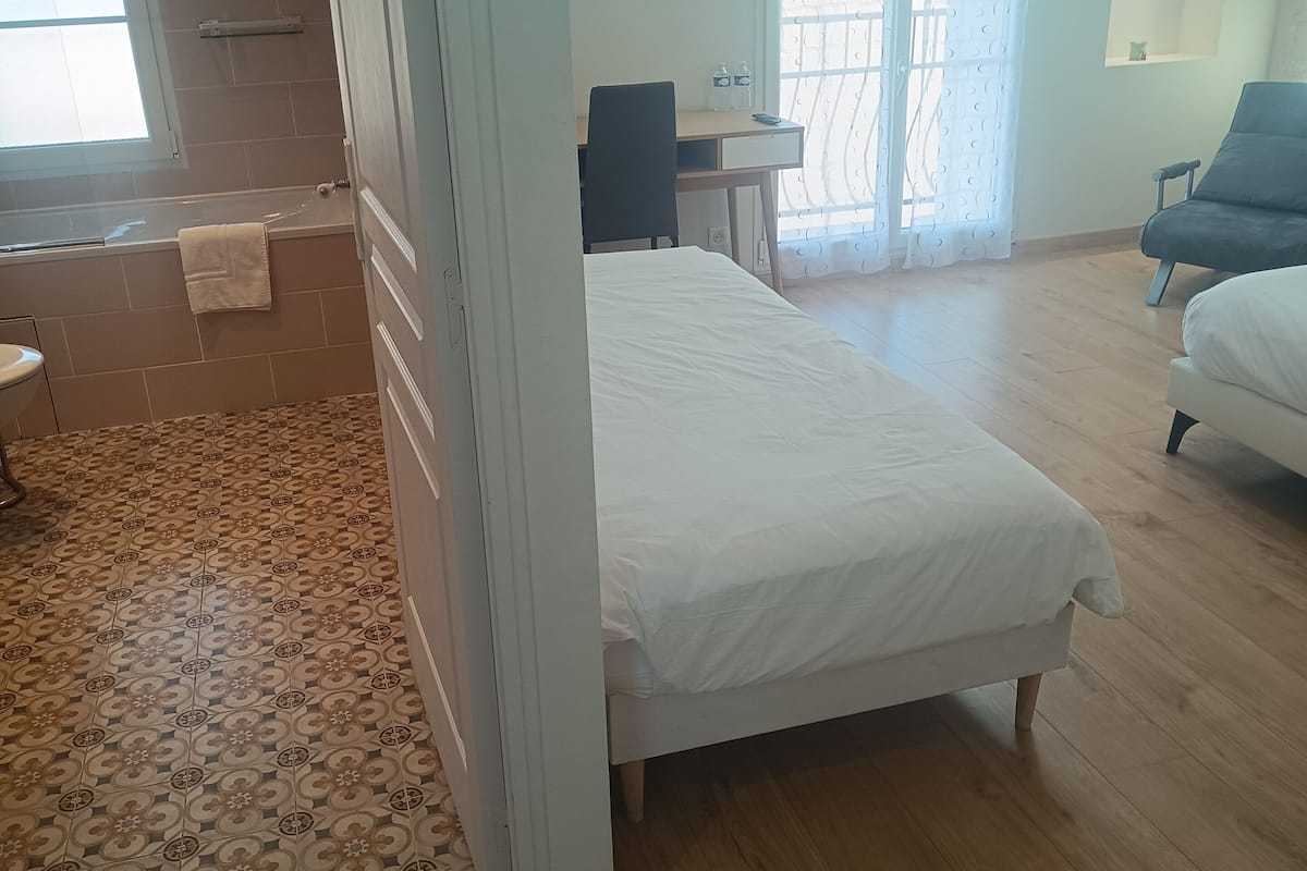 Een slaapkamer met een bed, een bureau, een stoel, een bank en een badkamer met bad en toilet.