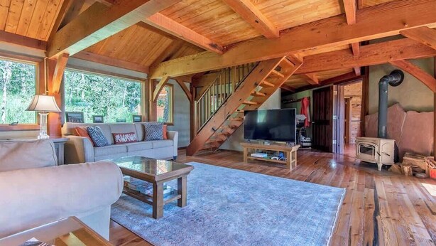 Amplio espacio tipo loft con techo de madera, televisor grande, sofá y escalera que conduce a un nivel superior.