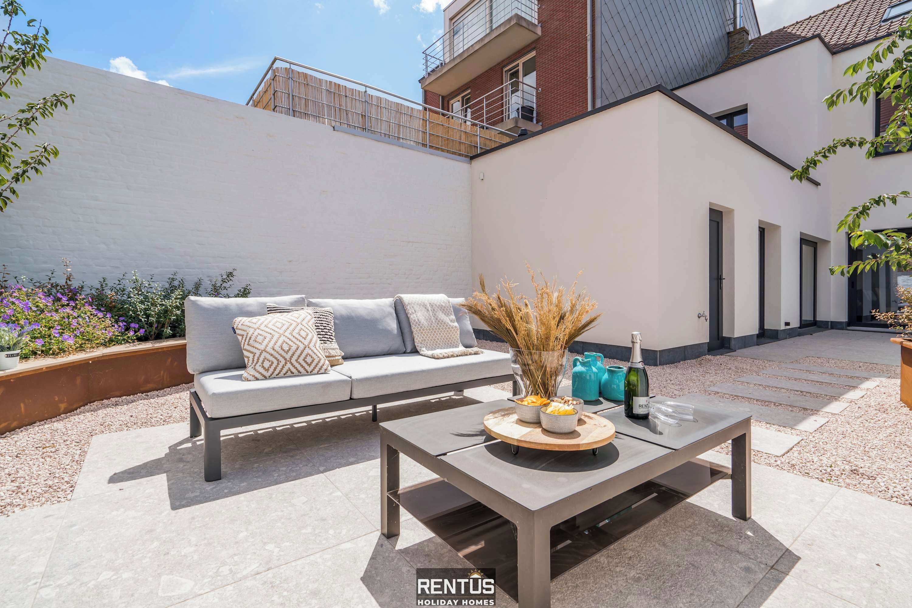 Een modern buitenpatio met een bank, een tafel met decoratieve objecten, en een wijnfles.