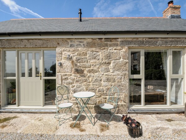 A stone house with a tiled roof, a white door, and a window with a view of the garden. - The Forge (Falmouth)