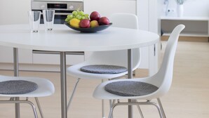 A modern kitchen with white cabinets, a round dining table with two chairs, and a bowl of fruit on the table.