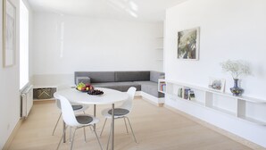 A modern living room with a white sofa, a dining table with chairs, and a bookshelf.