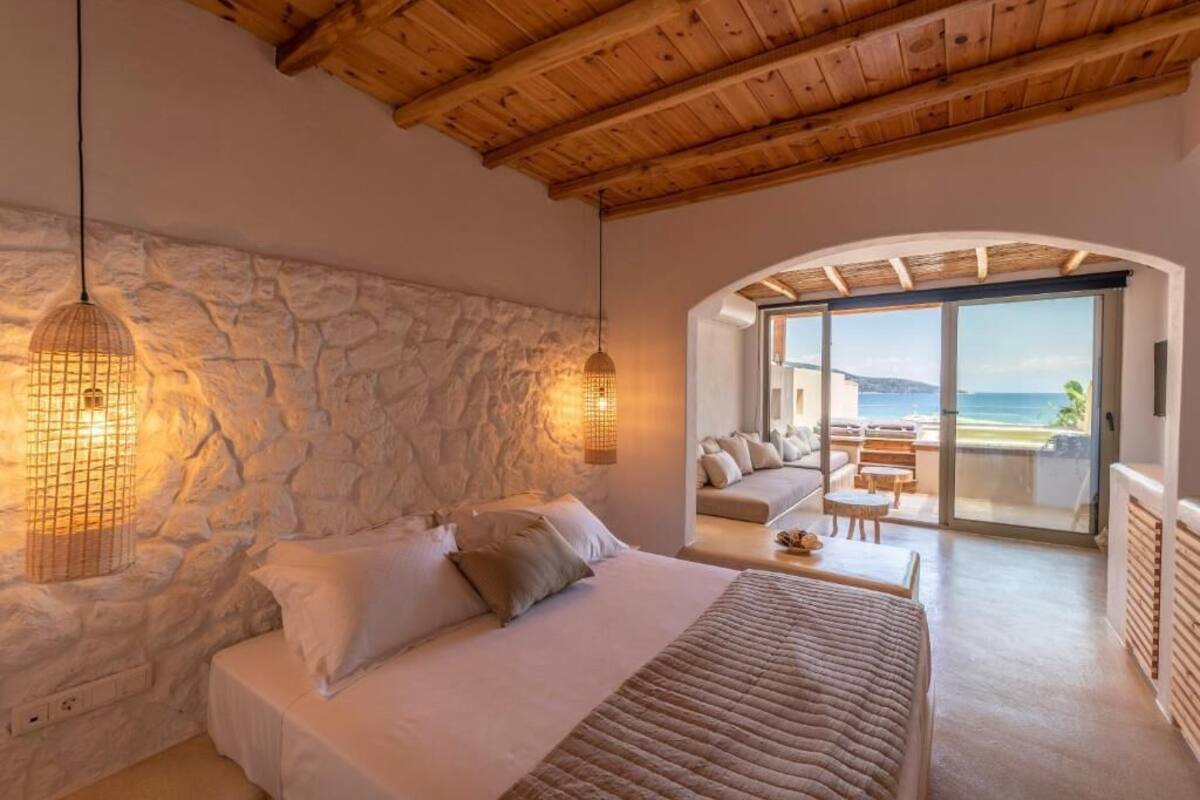 Un dormitorio con pared de piedra, una cama, una lámpara colgante y vistas al mar a través de un ventanal.