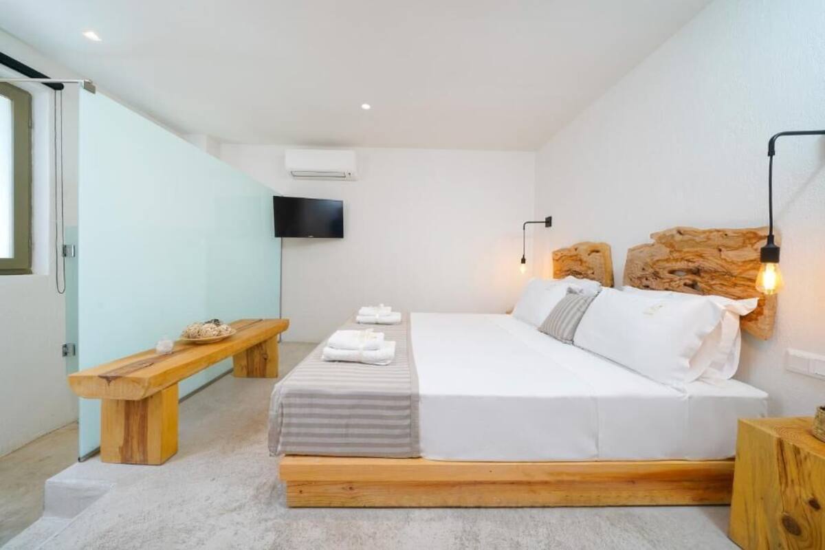 Un dormitorio moderno con una cama de madera, un banco, un televisor de pantalla plana y una pared de acento de piedra.