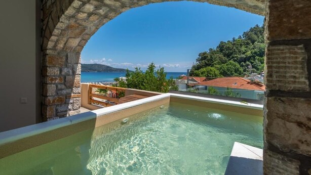 Arcada de pedra que dá acesso a uma piscina no terraço, com vista ampla do mar e da paisagem circundante.