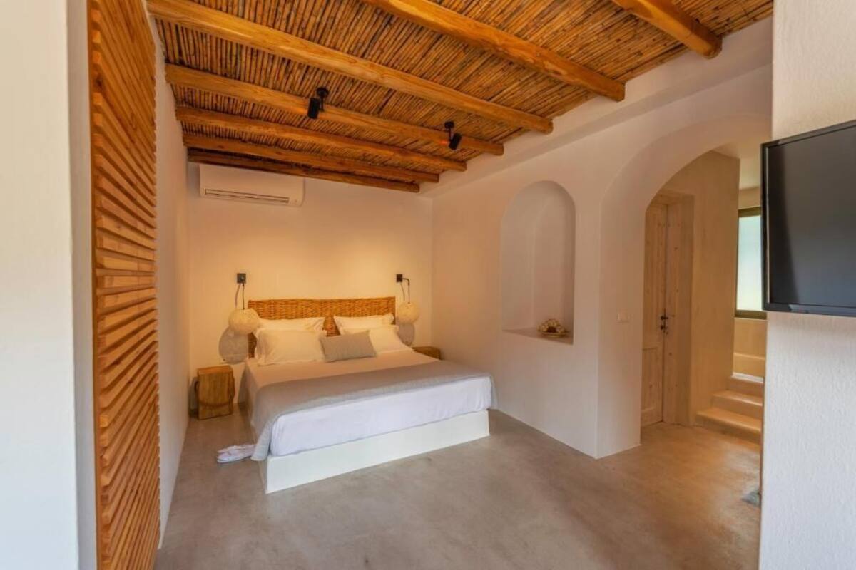 Un dormitorio con techo de madera, una cama con sábanas blancas, una mesita de noche y un televisor montado en la pared.