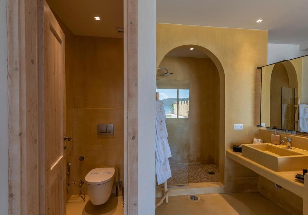 A modern bathroom with a wooden shower enclosure, a large mirror, and a visible outdoor view through the shower door.