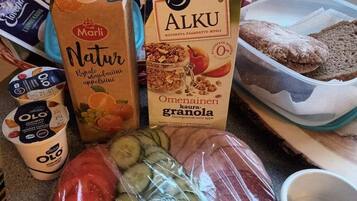 Una encimera de cocina con diversos alimentos, incluyendo un cartón de yogur Marli Natur, un cartón de Alku, un recipiente con granola, una bolsa de plástico con verduras y un bol de huevos.