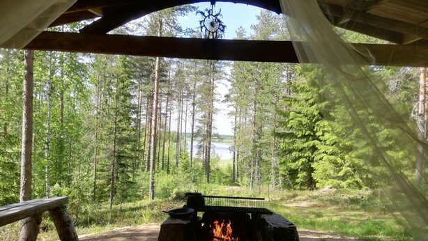 Eine rustikale Holzhütte mit einem Feuerkorb in der Mitte, umgeben von einem Wald.