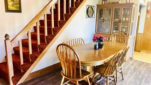 Un comedor con mesa y sillas de madera, una escalera con barandillas de madera y un mueble de madera con puertas de cristal.