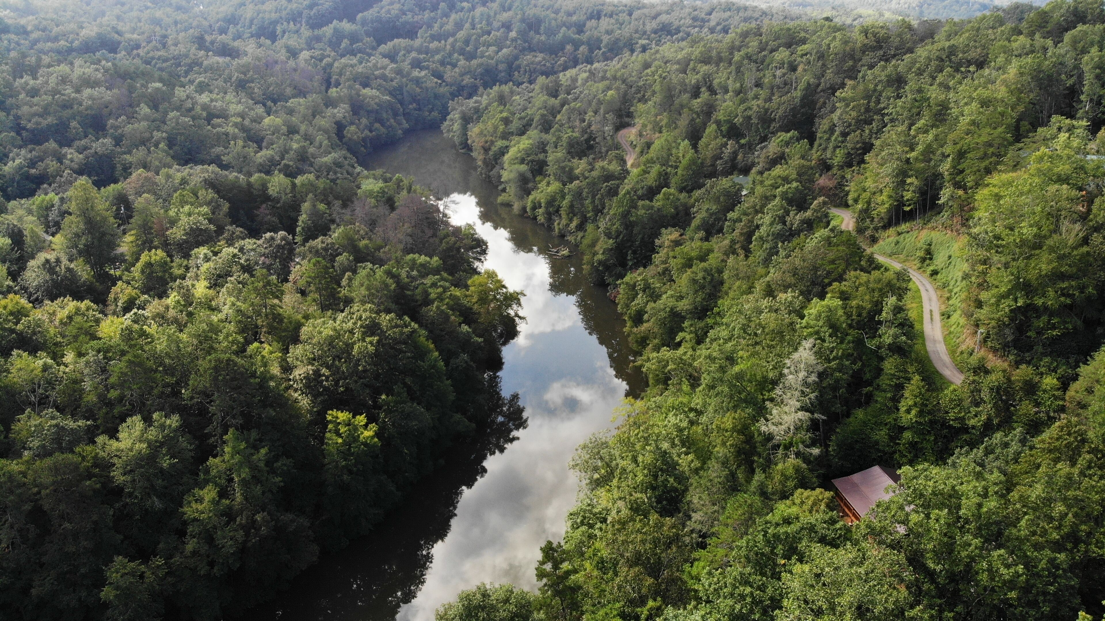 Vista aérea de un área boscosa con un río, una carretera sinuosa y un edificio pequeño.