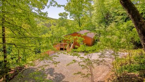 Eine Hütte, umgeben von dichtem Wald, mit einem Schotterweg, der zu einer Holzterrasse führt.