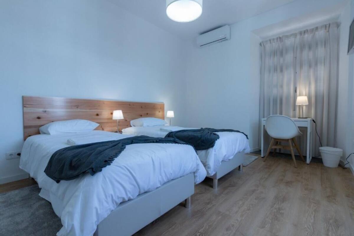 Habitación de hotel con dos camas, un escritorio, una silla y una ventana con cortinas.