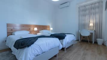 A hotel room with two beds, a desk, a chair, and a window with curtains.