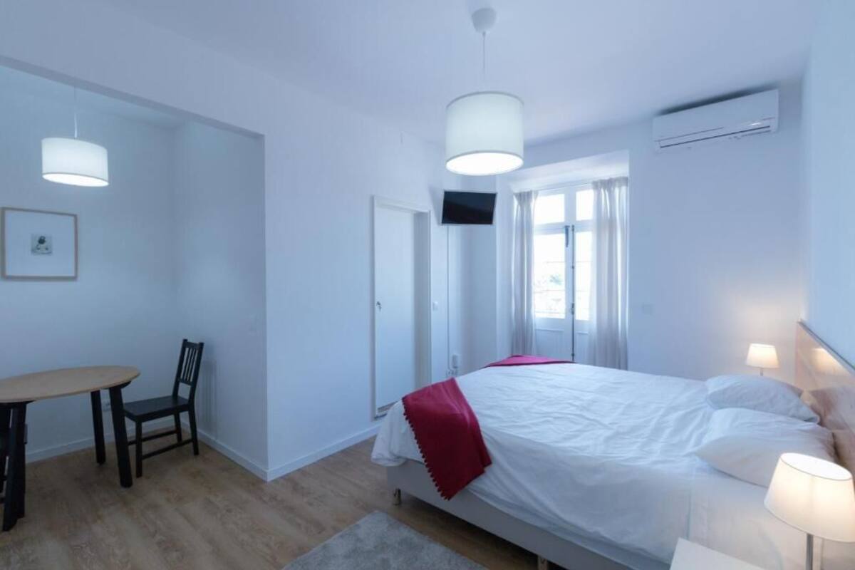 Un dormitorio con cama, mesita de noche, silla y escritorio con otra silla.