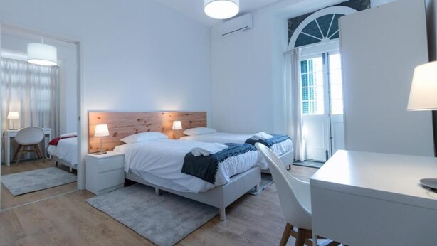 Un dormitorio moderno con cabecera de madera, dos camas, un escritorio y una silla.