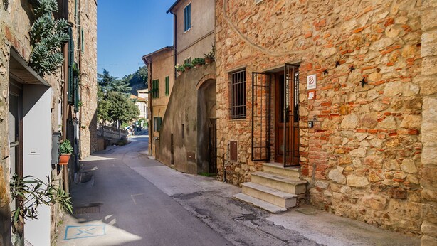Una calle estrecha con edificios de piedra, una entrada visible y un cielo azul despejado.