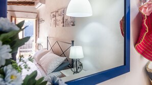 Un dormitorio con cama, una lámpara colgante blanca, una mesita de noche con lámpara y un espejo montado en la pared.