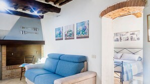 Un espacio de sala acogedor con un sofá, una mesita y una chimenea. Hay tres cuadros en la pared y una cama con cabecera.