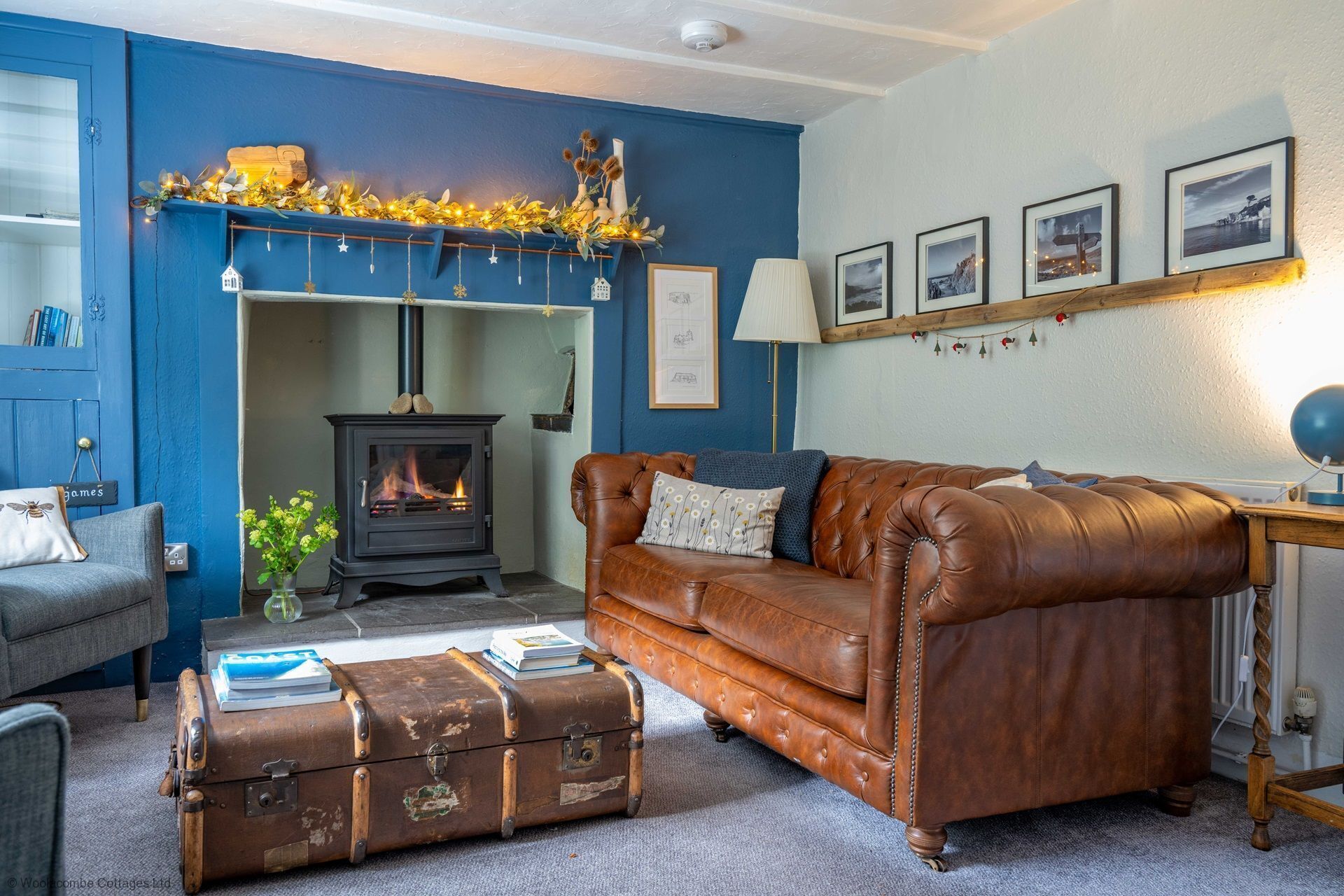 Een gezellige woonkamer met een blauwe muur, een open haard, een leren bank en een vintage koffer.