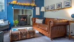 Ein gemütliches Wohnzimmer mit blauer Wand, Kamin, Ledersofa und einem alten Koffer.