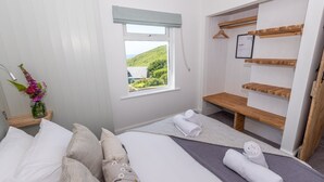 Ein Schlafzimmer mit zwei Betten, einem Fenster mit Blick auf Grünflächen, einem Holzboden mit einem gerahmten Bild und einer Vase mit Blumen.