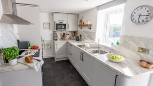 Eine moderne Küche mit weißen Schränken, einer Edelstahl-Spüle, einer Mikrowelle und einer Uhr an der Wand.