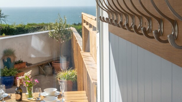 Ein Holz-Sitzbereich im Freien mit Blick auf das Meer, ein Metallkleiderständer und Kübelpflanzen.
