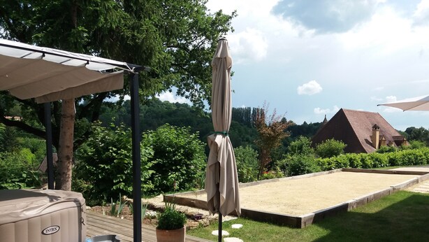 En trädgård med en bubbelpool, utemöbler, en pergola med ett tak, en krukväxt och en gräsmatta med en kant av stenar.