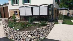 Ett hus med en trädgård, en uteplats och ett takförsett område med ett bord och stolar.