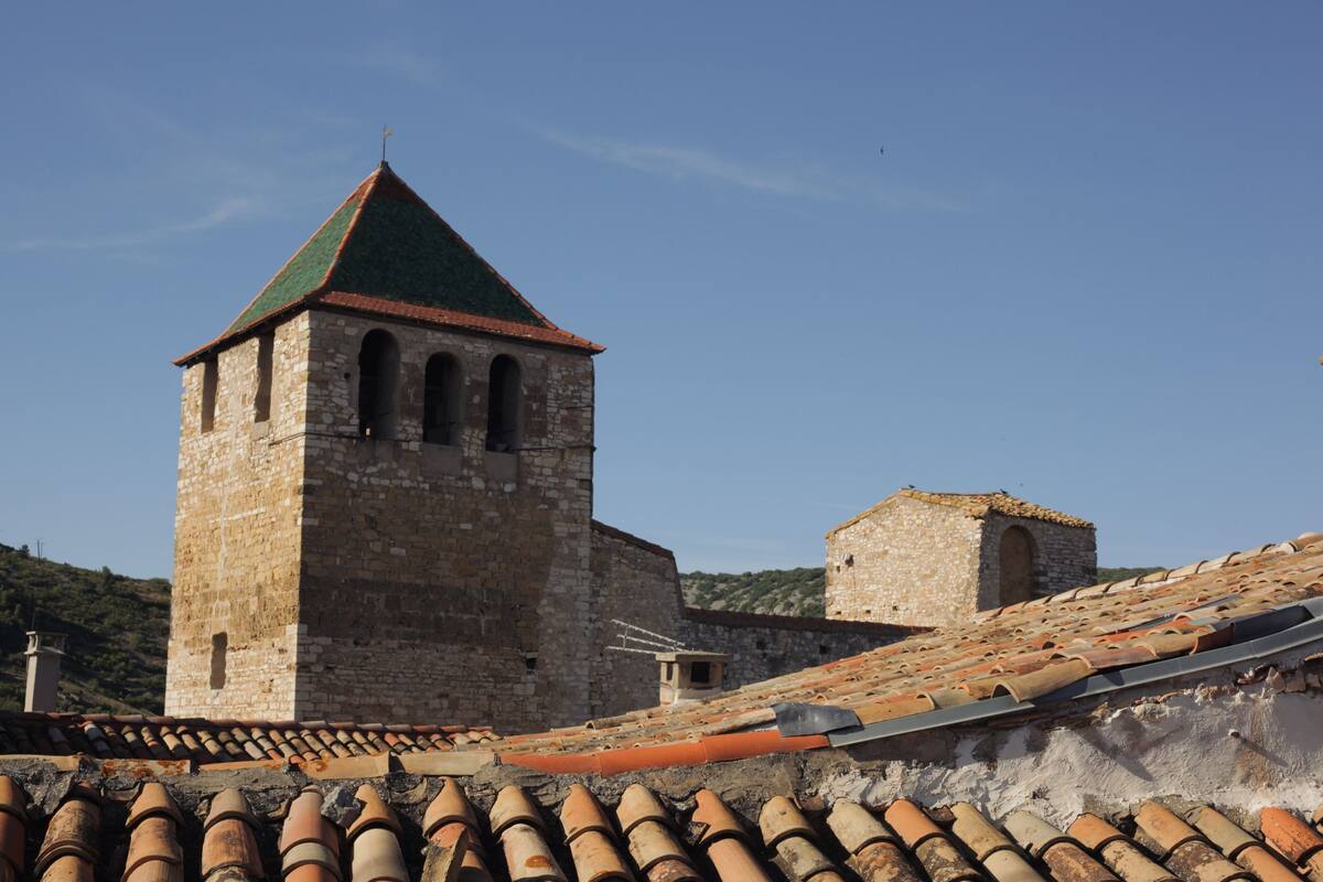 A stone tower with a green roof and a smaller adjacent building with a tiled roof.